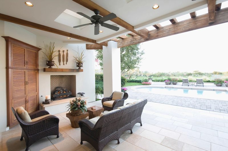 Covered patio with an outdoor fireplace and seating beside a pool